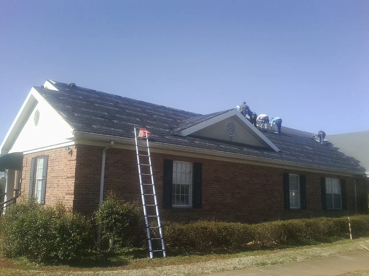 Crew tearing shingles off a brick ranch roof with a ladder set — Emergency Roof Repair work by our crew in Delphi Falls
