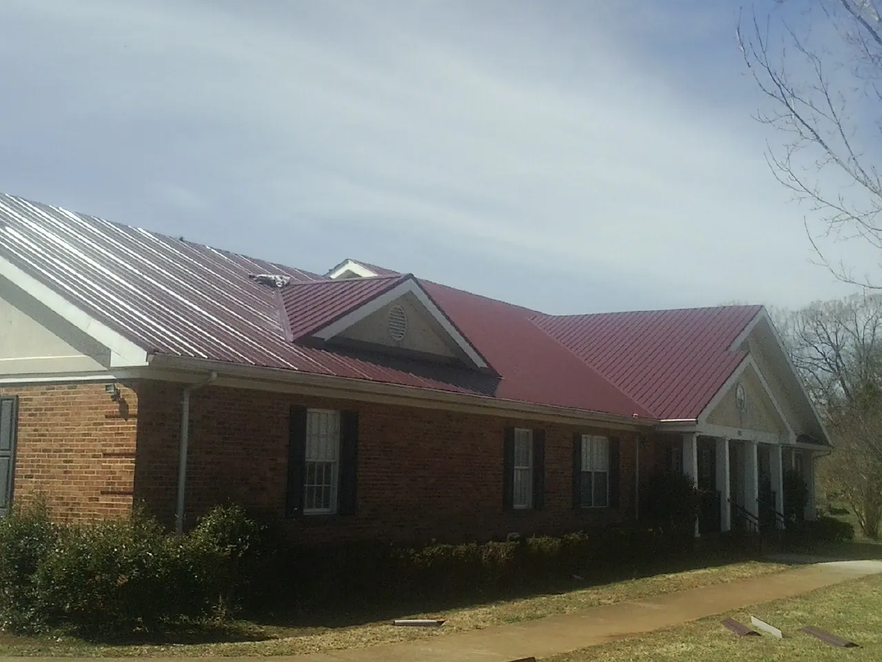 Red metal roof with gabled entries on a long brick building, from a Hail Damage Roof Repair job in Delphi Falls