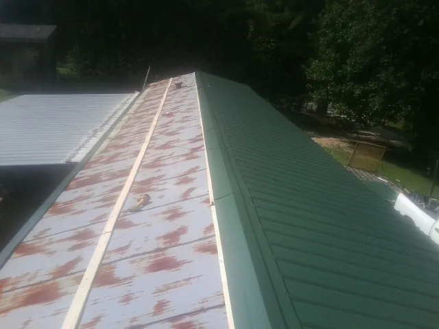 Old rusted panels beside newly installed green metal roofing — Wind Damage Roof Repair by Roofing Brothers in Delphi Falls