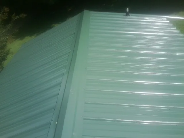 New green metal panels meeting at the ridge of a roof — Flat Roof Repair work by our crew in Delphi Falls