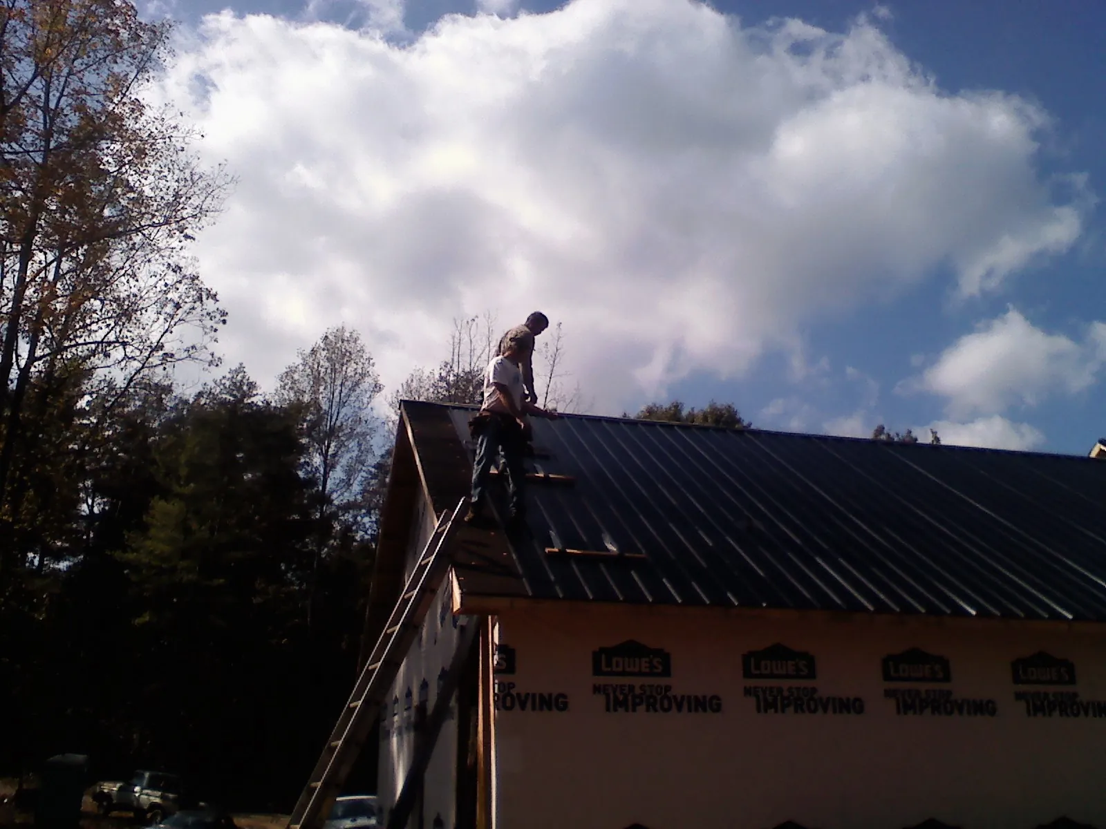 Roofer fastening dark metal panels high against a cloudy sky, from a Roof Inspection job in Delphi Falls