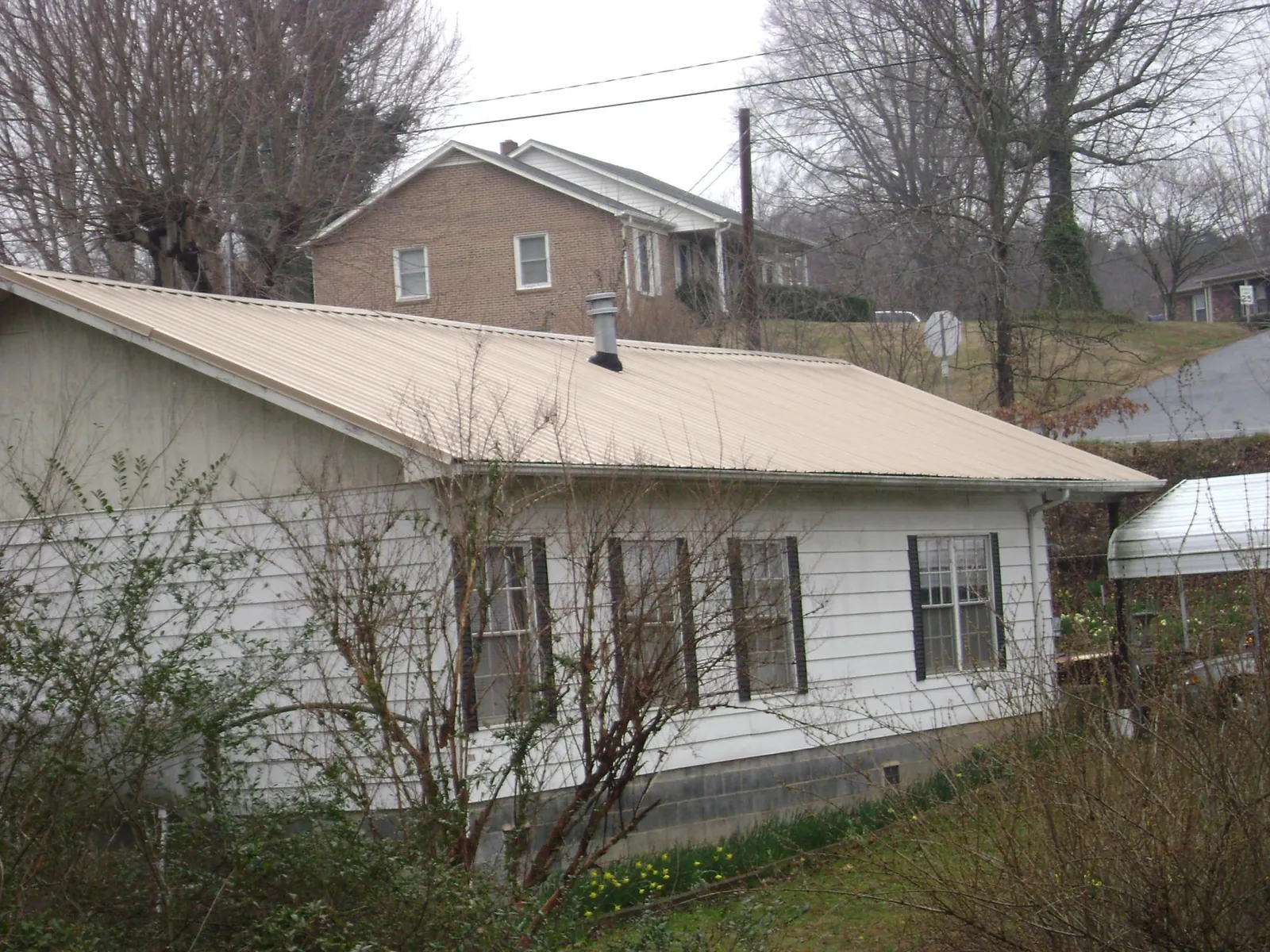Tan metal roof on a white sided house set into a hillside — Commercial Roofing by Roofing Brothers in Delphi Falls