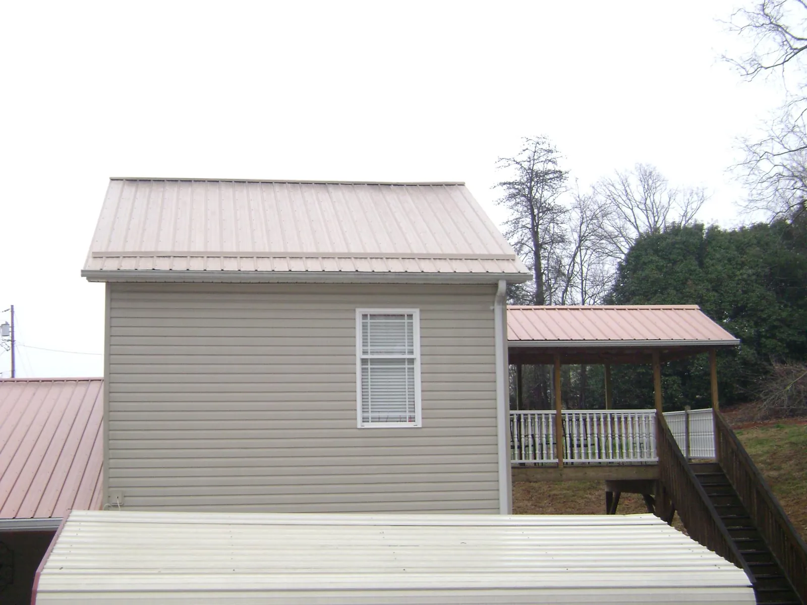 Tan metal roofs on a two story addition and attached porch, from a Roof Replacement job in Delphi Falls
